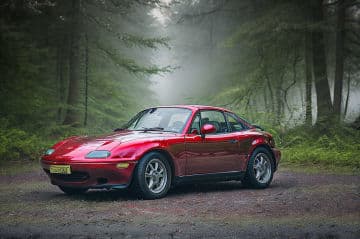 A red sports car parked in the middle of a forest A red sports car parked in the middle of a forest